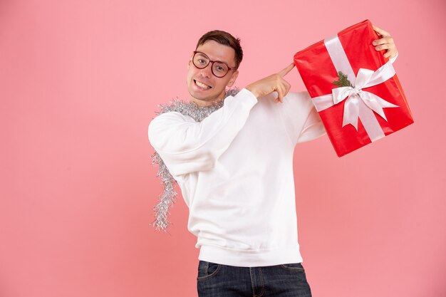 Vista frontal del joven sosteniendo el regalo de Navidad en la pared rosa