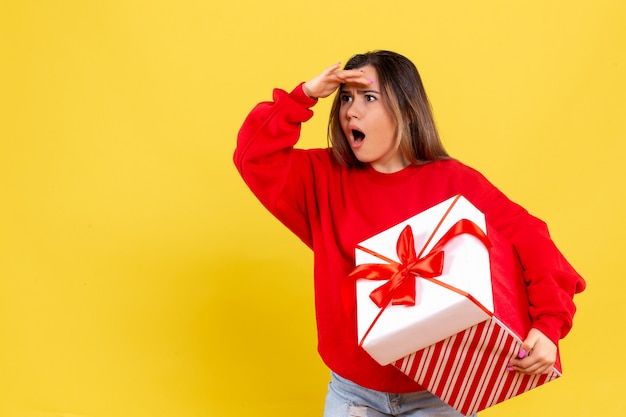 Vista frontal joven sosteniendo un regalo de Navidad sorprendentemente mirando a distancia sobre fondo amarillo