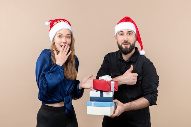 Vista frontal del joven sosteniendo regalos de Navidad con mujer en la pared rosa