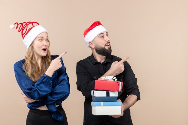 Vista frontal del joven sosteniendo regalos de Navidad con mujer en la pared rosa