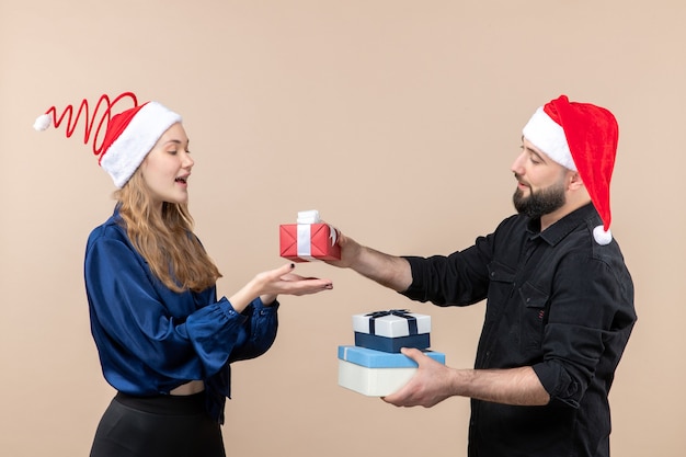 Vista frontal del joven sosteniendo regalos de Navidad con mujer en la pared rosa