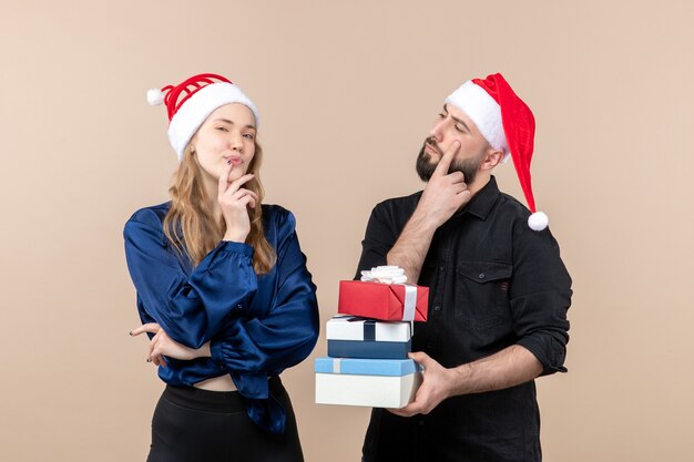 Vista frontal del joven sosteniendo regalos de Navidad con mujer en la pared rosa