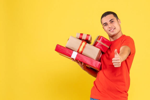 Foto gratuita vista frontal del joven sosteniendo regalos de navidad en la pared amarilla