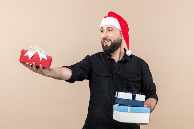 Vista frontal del joven sosteniendo regalos navideños y dándolos en la pared rosa