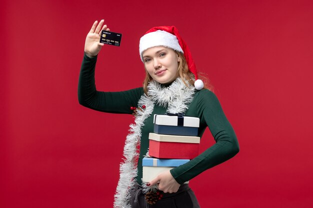 Vista frontal joven sosteniendo regalos y tarjeta bancaria en el escritorio rojo