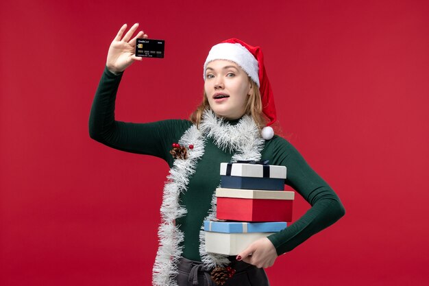 Vista frontal joven sosteniendo regalos y tarjeta bancaria sobre fondo rojo.
