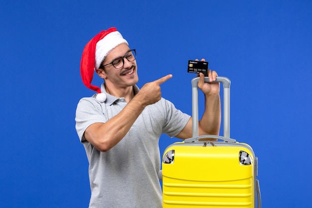 Vista frontal joven sosteniendo la tarjeta bancaria bolsa amarilla en la pared azul viaje emoción vacaciones