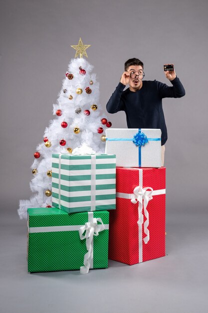 Vista frontal joven sosteniendo una tarjeta bancaria en el escritorio gris Navidad presente de año nuevo