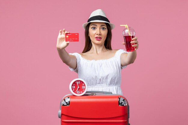 Vista frontal joven sosteniendo una tarjeta bancaria y jugo de vacaciones en la pared rosa claro viaje viaje vacaciones de verano mujer