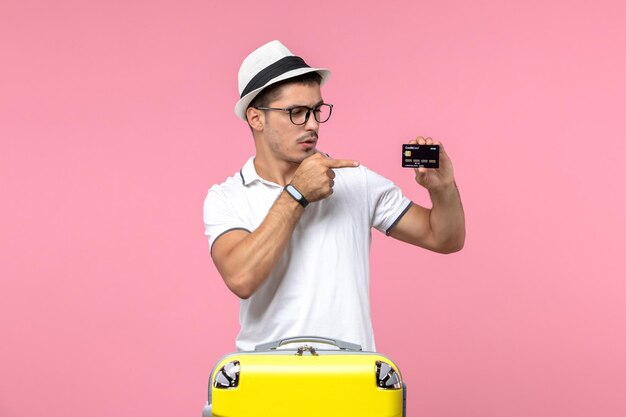 Vista frontal del joven sosteniendo una tarjeta bancaria negra en la pared rosa