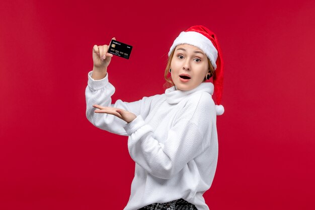 Vista frontal joven sosteniendo una tarjeta bancaria en el piso rojo rojo Navidad dinero de vacaciones