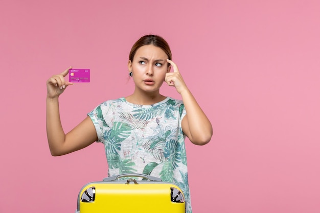 Vista frontal joven sosteniendo una tarjeta bancaria púrpura de vacaciones en el escritorio rosa viaje color vacaciones mujer viaje de verano