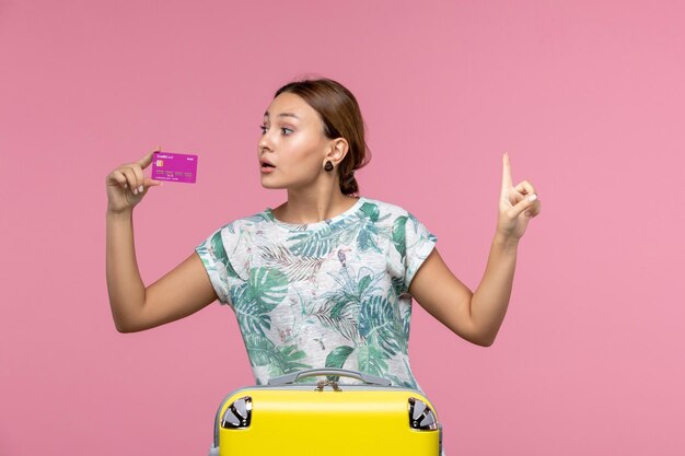 Vista frontal joven sosteniendo una tarjeta bancaria púrpura de vacaciones en el escritorio rosa viaje color vacaciones de verano mujer viaje