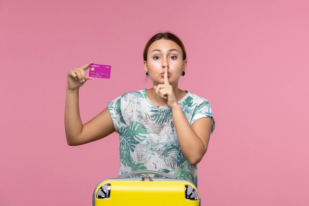 Vista frontal joven sosteniendo una tarjeta bancaria púrpura de vacaciones en la pared rosa claro viaje color vacaciones mujer viaje de verano