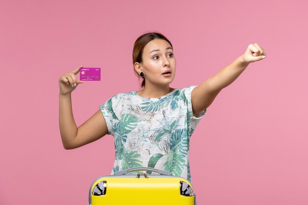 Vista frontal joven sosteniendo una tarjeta bancaria púrpura de vacaciones en la pared rosa verano descanso color viaje vacaciones mujer