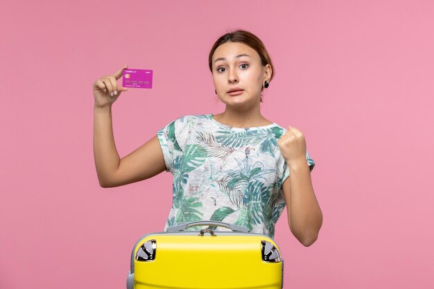 Vista frontal joven sosteniendo una tarjeta bancaria púrpura de vacaciones en la pared rosa viaje color vacaciones mujer viaje de verano