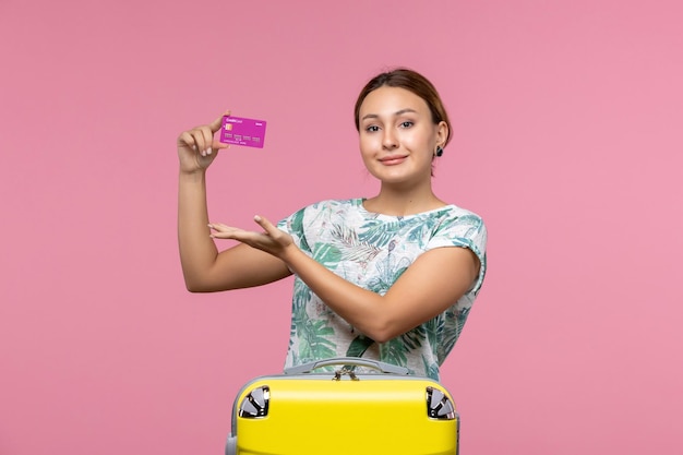 Vista frontal joven sosteniendo una tarjeta bancaria púrpura de vacaciones en la pared rosa viaje mujer vacaciones de viaje de verano