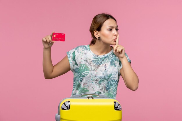 Vista frontal joven sosteniendo una tarjeta bancaria roja en la pared rosa vuelo mujer viaje avión resto