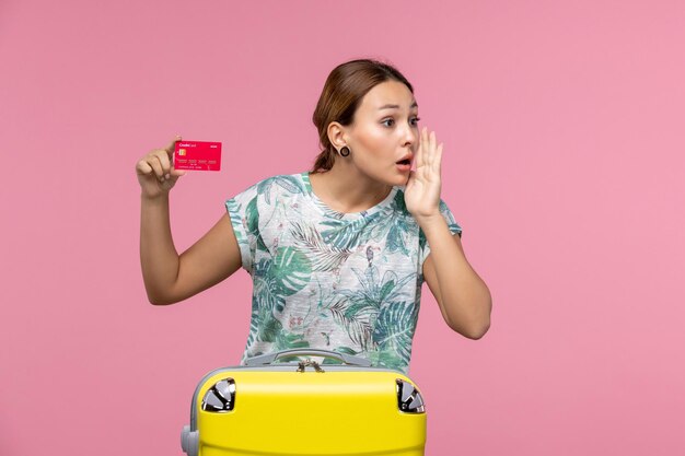 Vista frontal joven sosteniendo una tarjeta bancaria roja en la pared rosa vuelo mujer viaje avión resto