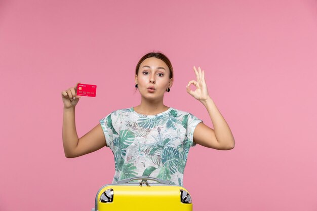 Vista frontal joven sosteniendo una tarjeta bancaria roja en la pared rosa vuelo mujer viaje avión vacaciones descanso