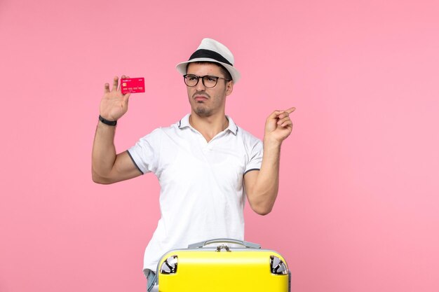 Vista frontal del joven sosteniendo una tarjeta bancaria roja en la pared rosa