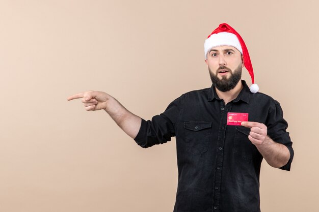 Vista frontal del joven sosteniendo una tarjeta bancaria roja en la pared rosa