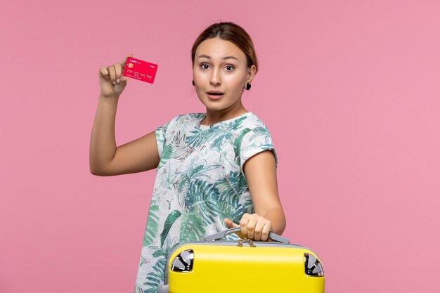 Vista frontal joven sosteniendo una tarjeta bancaria roja en la pared rosada mujer de descanso de avión de viaje de vuelo