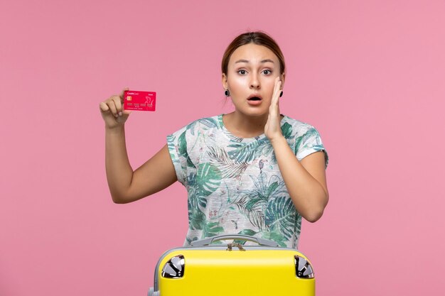 Vista frontal joven sosteniendo una tarjeta bancaria roja y susurrando sobre la pared rosa vuelo mujer viaje avión vacaciones descanso