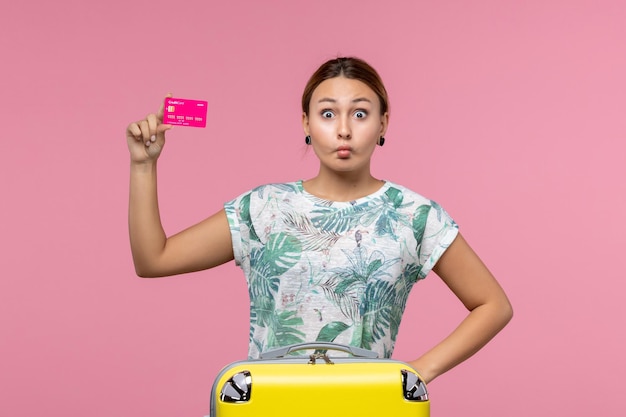 Vista frontal joven sosteniendo una tarjeta bancaria de vacaciones en la pared rosa mujer viaje en avión vuelo vacaciones resto