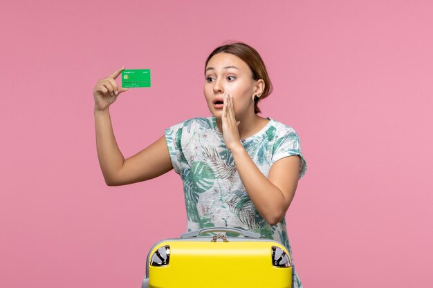 Vista frontal joven sosteniendo una tarjeta bancaria de vacaciones en la pared rosa viaje de viaje de verano descanso mujer vacaciones