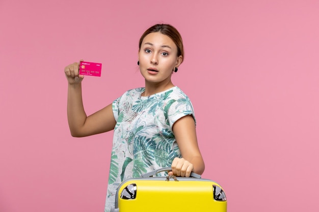 Vista frontal joven sosteniendo una tarjeta bancaria de vacaciones en la pared rosada viaje en avión vuelo vacaciones mujer resto