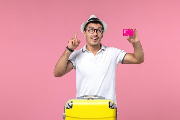 Vista frontal del joven sosteniendo una tarjeta bancaria en las vacaciones de verano en la pared de color rosa claro