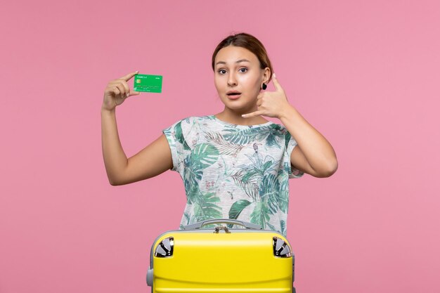 Vista frontal joven sosteniendo una tarjeta bancaria verde de vacaciones en la pared rosa claro viaje mujer descanso viaje verano