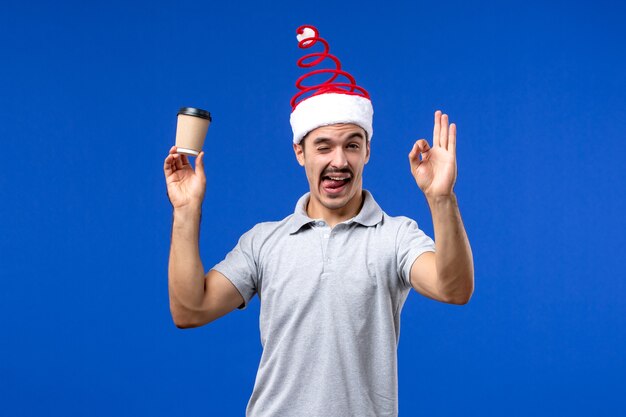 Vista frontal joven sosteniendo una taza de café de plástico en el escritorio azul vacaciones masculinas de año nuevo