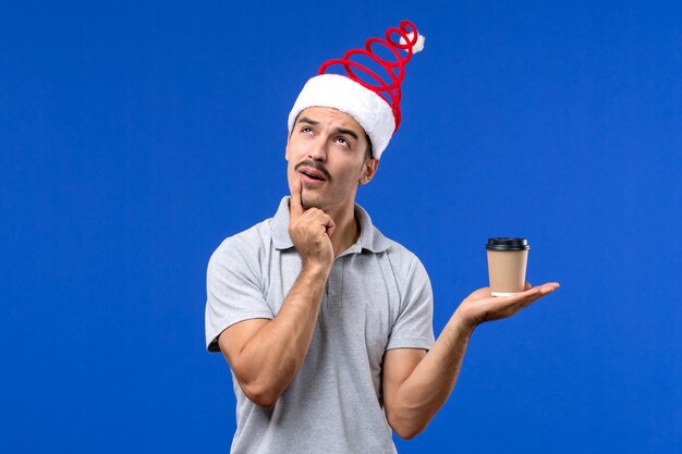 Vista frontal joven sosteniendo una taza de café de plástico en la pared azul emoción año nuevo masculino