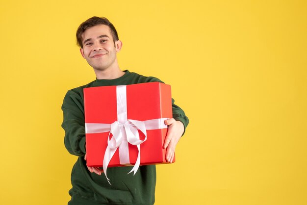 Vista frontal joven con suéter verde mostrando su regalo en amarillo