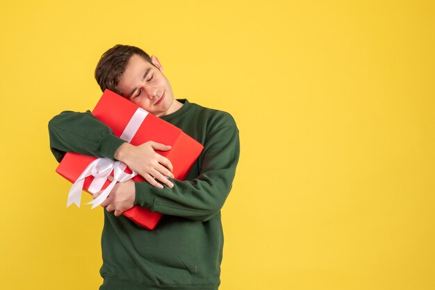 Vista frontal joven con suéter verde sosteniendo su regalo firmemente en amarillo