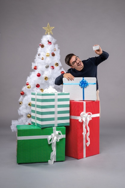 Vista frontal joven con tarjeta bancaria en piso gris año nuevo presente Navidad