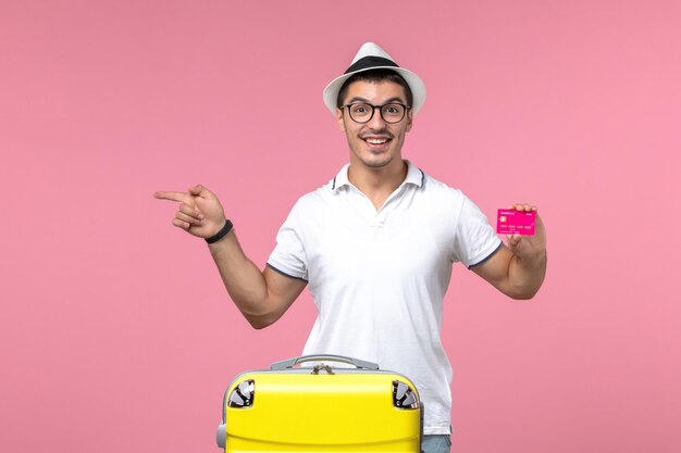 Vista frontal del joven con tarjeta bancaria en vacaciones de verano en la pared rosa