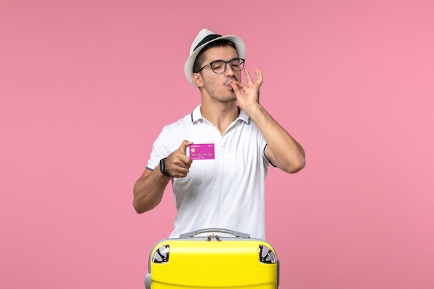 Vista frontal del joven con tarjeta bancaria en vacaciones de verano en la pared rosa
