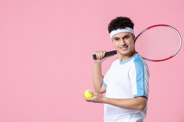 Vista frontal joven tenista en raqueta de ropa deportiva en pared rosa