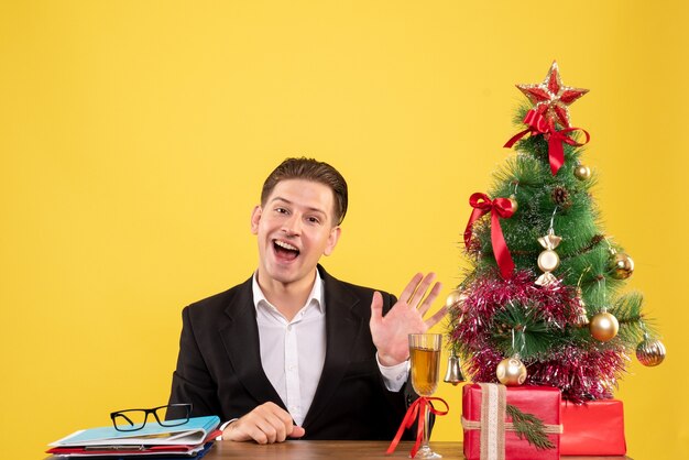 Vista frontal joven trabajador sentado con regalos de Navidad y árbol