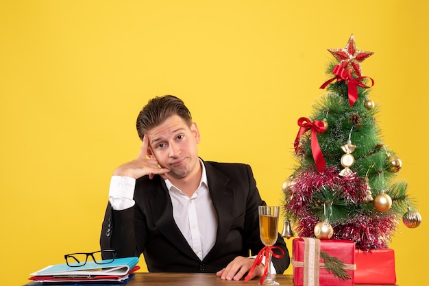 Vista frontal joven trabajador sentado con regalos de Navidad y árbol