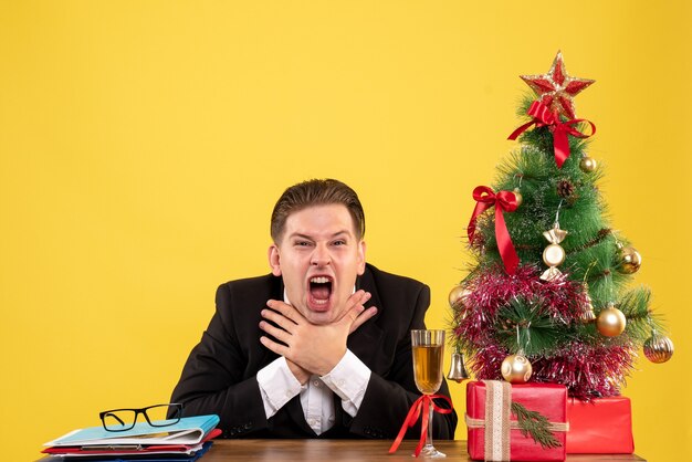 Vista frontal joven trabajador sentado con regalos de Navidad y árbol