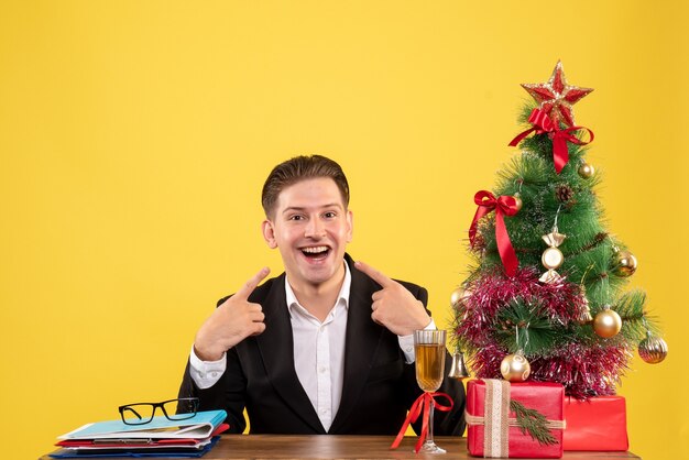 Vista frontal joven trabajador sentado con regalos de Navidad y árbol