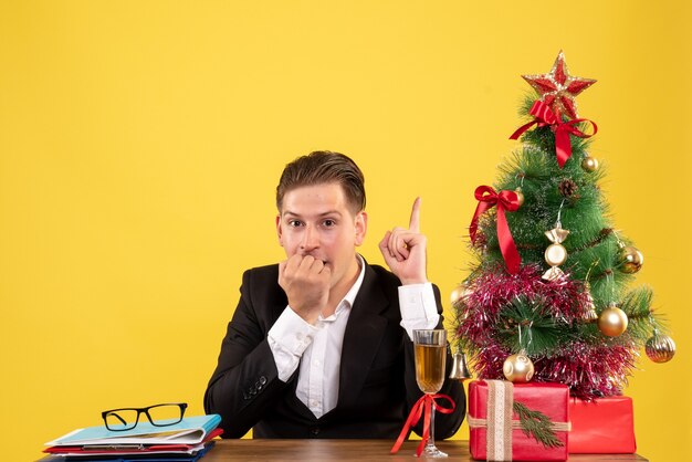 Vista frontal joven trabajador sentado con regalos de Navidad y árbol