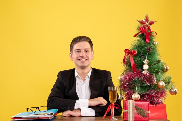 Vista frontal joven trabajador sentado con regalos de Navidad y árbol