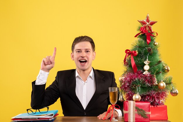 Vista frontal joven trabajador sentado con regalos de Navidad y árbol