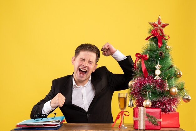 Vista frontal joven trabajador sentado con regalos de Navidad y árbol