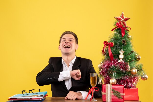 Vista frontal joven trabajador sentado con regalos de Navidad y árbol